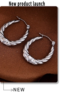 Macro detail of silver twisted C-hoop earrings on a premium brown leather texture