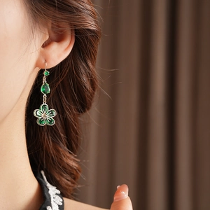 Close-up of silver flower and green teardrop zircon earrings worn by a model