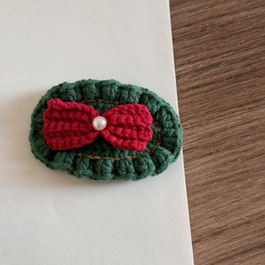 Macro detail of crochet Christmas hair clip with green base, red bow and white pearl