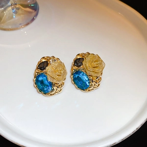 Macro shot of blue gemstone floral earrings with gold rose details on a white plate
