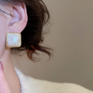 Detail of elegant gold-plated square shell earrings worn by a model in warm light