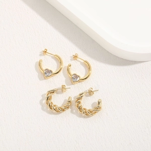 Detail of 14K gold-plated twisted hoop earrings and heart zircon charms on white tray