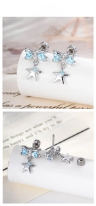 Macro shot of silver bow earrings with blue heart stones and hanging star pendants