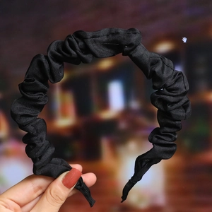 Detail view of a black pleated fabric headband held by hand with soft night background