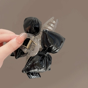 Detail of a large black glossy leather bow hair claw clip held in hand with clear details