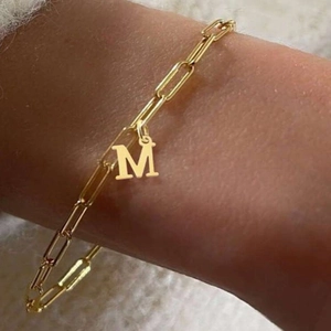 Detail of a gold-tone paperclip chain bracelet with a letter M pendant on a wrist