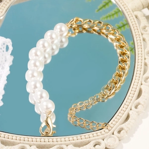 Detail of baroque pearl and chunky gold chain mixed bracelet on a vintage mirror