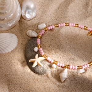 Pink and gold beaded beach anklet with starfish and shell charms on natural sand