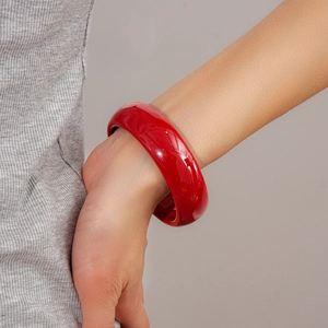 Gros plan d'un large bracelet jonc en résine rouge brillant porté au poignet d'une femme
