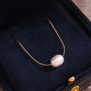 Detailed close-up of a single oval pearl necklace on a gold chain in a velvet jewelry box