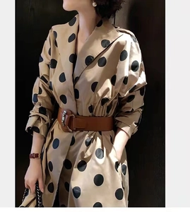 Detail of a brown leather wide belt with a metallic buckle on a beige polka dot coat