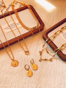 Detail of vintage gold M-pendant necklace with colorful beads and textured coin earrings