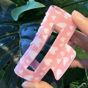 Detailed close-up of a square pink hair claw clip with white heart patterns held in hand
