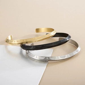 Detail of three C-shaped titanium steel bangles in gold, black and silver with engraved textures