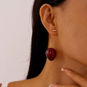 Close-up of red cherry acrylic earrings with glitter on a model for a sweet summer look