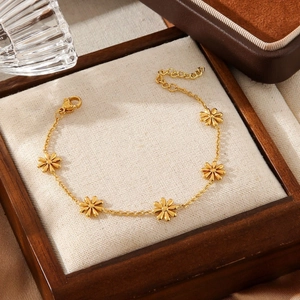 Elegant gold stainless steel daisy bracelet with floral charms on a beige fabric display