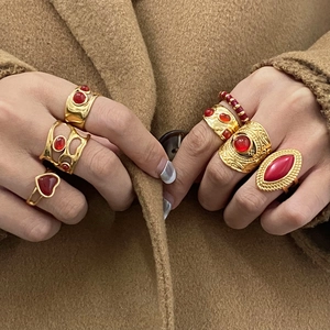 Detail of six vintage gold-plated rings with red stones worn against a camel coat