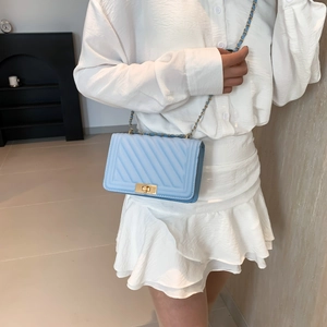 Detail of light blue chain bag with V-quilted texture and gold metal clasp on model
