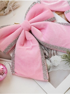 Close-up of pink velvet Christmas bow with silver glitter edges on festive background