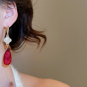 Detailed view of silver needle drop earrings featuring a red pear-shaped crystal pendant