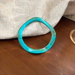 Detail view of a wavy teal resin bangle bracelet with modern artistic water ripple design