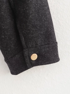 Detail of dark grey wool jacket cuff with a smooth gold metallic button close-up