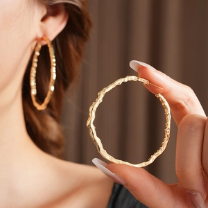 Détail macro de boucles d'oreilles créoles dorées avec texture martelée et éclat métallique