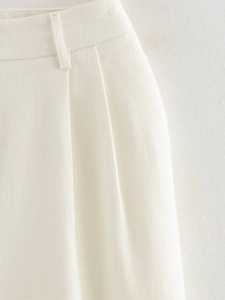Detailed close-up of white linen trousers featuring belt loops and pleated waist design