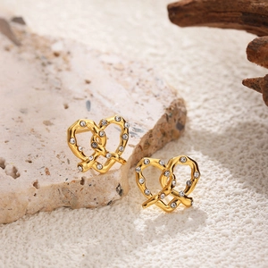 Macro shot of 18K gold pretzel-shaped earrings with clear crystals on a stone surface