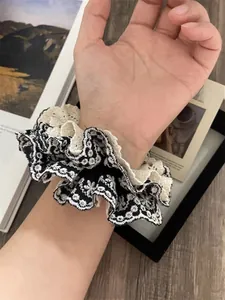 Detail of layered white lace and floral embroidery scrunchie worn on a wrist