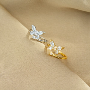 Detailed shot of gold and silver butterfly rings with sparkling zircon on beige silk