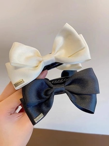 Detail of black and beige ribbon bow hair clips with textured fabric and gold metal tags