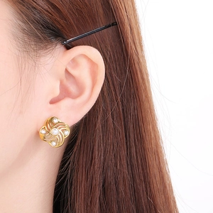 Close-up of a model wearing a gold flower pearl earring with a spiral shell design