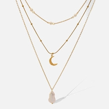 Detail of layered gold necklace with moon pendant and white baroque pearl charm