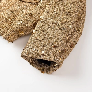 Dettaglio macro delle paillettes dorate e del tessuto a trama sulla manica della giacca