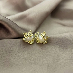 Elegant gold owl stud earrings featuring white pearls and sparkling rhinestone details