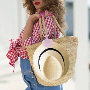 Pink heart-shaped PU leather hat clip for travel attached to a straw tote bag