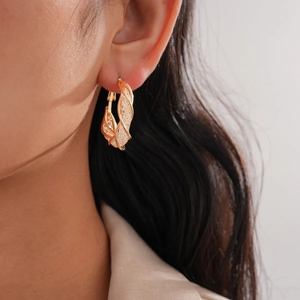Close-up of a gold-plated twisted hollow hoop earring worn by a model with elegant texture