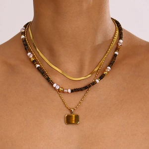 Detail of layered gold necklace featuring pearl beads and tiger eye stone pendant