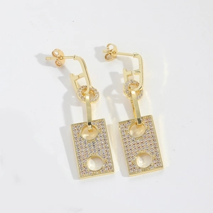 Close-up of geometric gold earrings with pink zircons and hollow rectangular pendant