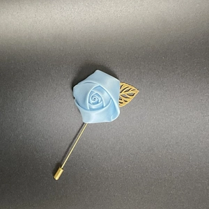 Close-up of light blue fabric rose brooch with golden hollow leaf and long stick pin