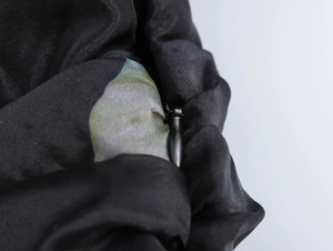 Dettaglio della cerniera invisibile su piumino in raso nero con trama del tessuto lucido