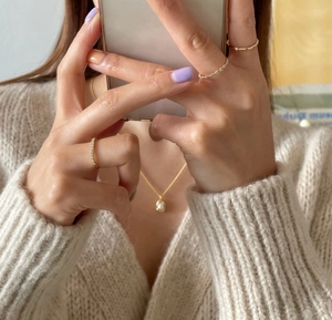 Close-up of pearl pea necklace and gold minimalist rings with warm cozy aesthetic