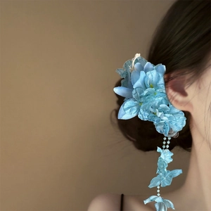 Detail view of a blue fabric flower hair clip with elegant tassels worn on dark hair