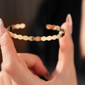 Macro shot of polished gold open bracelet with elegant scalloped wave edge design