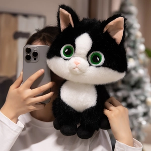 Plush black and white cat doll with green eyes being held in a cozy indoor setting