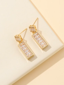 Elegant gold square earrings with rectangular cubic zirconia stones on cream leather