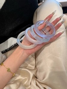 Détail de quatre joncs translucides en œil de chat avec un bracelet chaîne à cœurs