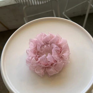 Detail shot of a pink pleated lace hair scrunchie placed on a white ceramic plate
