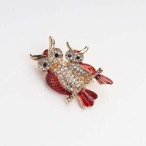 Detail of owl brooch with red enamel and sparkling rhinestones on golden metal branch